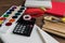 Angled view over a wooden desk with school supplies on it. Stepler, colored pencils, notebooks, calculator, scissors, tapes, paint