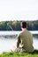 Angler sitting in grass at lake fishing with his rod