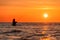 An angler in waterproof trousers fishes in front of a gorgeous orange sunset in the Baltic Sea.