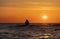 An angler in waterproof trousers fishes in front of a gorgeous orange sunset in the Baltic Sea.