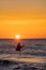 An angler in waterproof trousers fishes in front of a gorgeous orange sunset in the Baltic Sea.