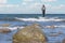 An angler in waterproof trousers is fishing in the Baltic Sea. He is standing on a stone in the water