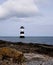 Anglesey lighthouse, rocky foreground, dogs playing on seashore, Wales