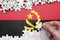 Angola flag is depicted on a table on which the human hand folds a puzzle of white color