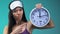 Angry Asian woman in pajamas and eye mask pointing finger at clock time to sleep