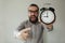 Angry boss with beard holds alarm clock screaming on camera