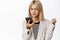 Angry corporate woman, business girl looking at mobile phone with furious face and frowning grimace, standing over white