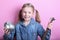 Angry funny young girl with silver piggy bank and hammer on pink background. save money concept.