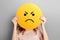 angry . Girl holds a yellow smiley with aggressive face  on a grey background
