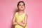 An angry little girl wearing yellow dress standing with crossed arms posing over pink background. Displeased preschooler child