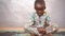 Angry Looking Little African Boy Sitting Legs Crossed On A Mat With His Fists Clenched