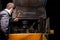 An angry male mechanic is repairing the engine of an old truck with an open hood hitting it with a hammer