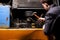 An angry male mechanic is repairing the engine of an old truck with an open hood hitting it with a hammer