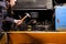 An angry male mechanic is repairing the engine of an old truck with an open hood hitting it with a hammer