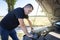 An angry man looks at the idle car engine. The driver tries to explain the cause of the breakdown to the mechanic using his