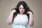 Angry plus size fashion model, fat woman on beige background, overweight female body