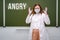 Angry school nurse in a medical mask on a blackboard background, copy space. Concept of problems at school during the coronavirus