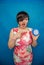 Angry screaming unhappy girl holding a round alarm clock on blue studio background