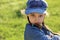 Angry serious kid girl in blue hat grimacing on summer green grass background. Closeup portrait