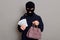 Angry serious thief dressed in balaclava and black turtleneck looks at camera and holds money and stolen women`s handbag, robbery
