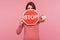 Angry strict woman in pink sweater holding stop warning sign and pointing finger at you, access forbidden, prohibition