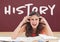 Angry student girl at table against red blackboard with history text