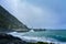 Angry waves breaking onto black sand beach of a small bay. A stormy day on the coastline of Cape Palliser near