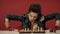 Angry woman sits at a table with chess, leaning her hands on the table in the studio on a red background. The woman