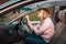 A angry woman is sitting behind the wheel of a right-handed car and shows a fist to the windshield