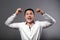 Angry young business man looking with aggressive eyes and waving the hands with fists above the head on grey background. Closeup