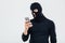 Angry young man in balaclava using cell phone