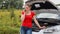 Angry young woman standing at broken vehicle and calling car repair service