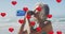 Animation of red heart balloons rising over woman drinking water on beach