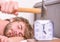 Annoying ringing alarm clock. Man bearded annoyed sleepy face lay pillow near alarm clock. Guy knocking with hammer