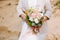 Anonymous bride with wedding bouquet close up at sandy beach.