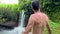 Anonymous brunet man standing near waterfall enjoying view in tropical paradise. Vacation in wild jungle to explore