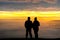 Anonymous couple standing on mountain together in love watching sunrise silhouetted stood high above clouds looking down valley