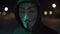 An anonymous hacker in a hood walks down the street and looks at the camera. Man with vendetta mask. 4K LOG