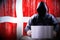 Anonymous hooded hacker, flag of Denmark, binary code - cyber attack concept