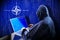Anonymous hooded hacker, flag of NATO, binary code - cyber attack concept