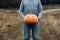 Anonymous Man in blue wear holds a carved orange Halloween pumpkin in front of him, outdoors.