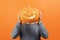 Anonymous Man in a sweater holds a carved Halloween pumpkin in front of his face on a orange background.