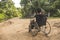 An anonymous paraplegic man on his old wheelchair staring far away. Traveling on a dirt road at a remote village