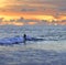 Anonymous silhouette of male or female surfer surfing and riding waves on sunset wild sea under a stunning orange sky in beauty ho