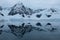 Antarctica mountains and glaciers reflect in mirror blue bay on cloudy day