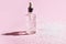 Anti aging serum in a glass bottle on a pink background with snow.