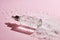 Anti aging serum in a glass bottle on a pink background with snow.