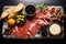 Antipasto platter with prosciutto crudo or jamon, ham, olives and baguette, top view of black marble cutting board with olives in