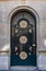 Antique arch door with mosaic rosettes and stone block wall of old building in Paris France. Vintage metal and matte glass doorway