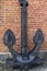 An antique black metal anchor with two large pointed legs standing on a gray stone
